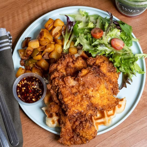 Fried chicken and waffles with a side of roasted potatoes, salad, and chili sauce.