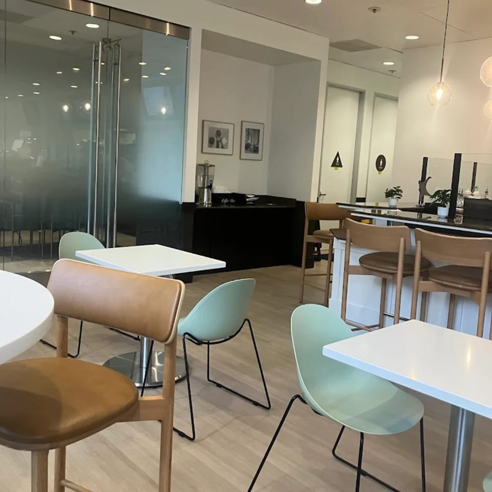 Modern cafe interior with light wood floors, white tables, and mint green and brown chairs.