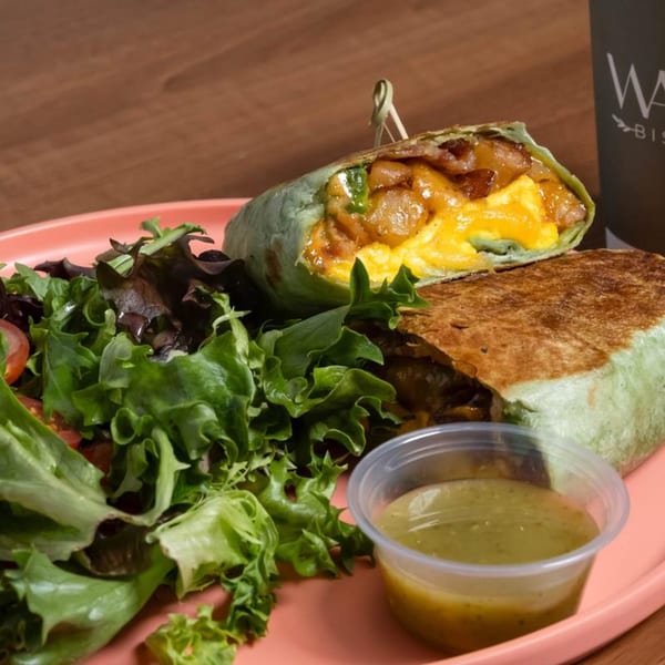 A breakfast burrito, cut in half, with a side salad and green dressing on a pink plate.