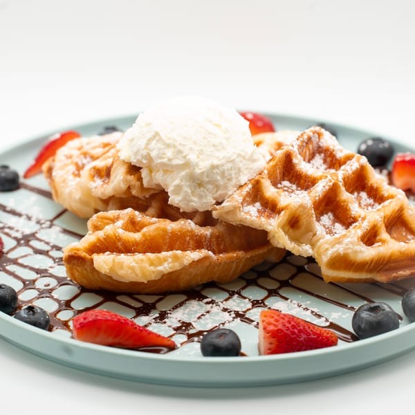 Golden waffles topped with vanilla ice cream, fresh strawberries, and blueberries on a blue plate.