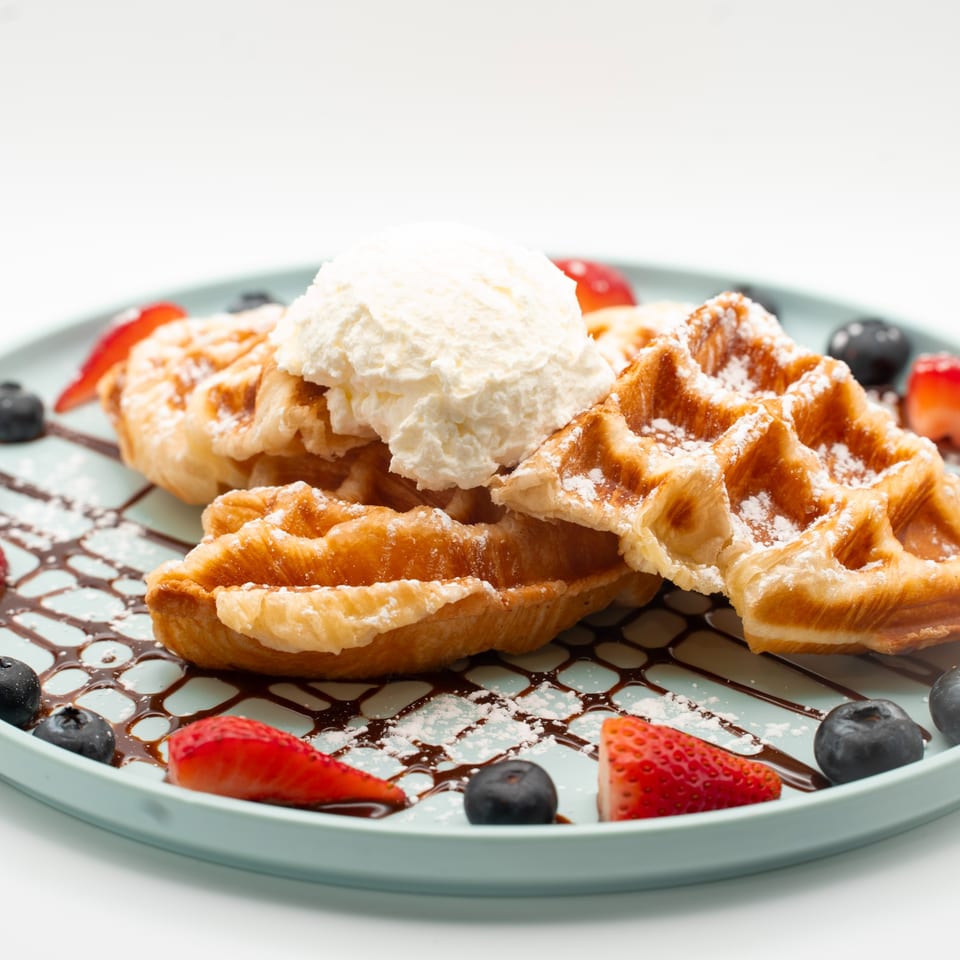 Golden waffles topped with vanilla ice cream, fresh strawberries, and blueberries on a blue plate.