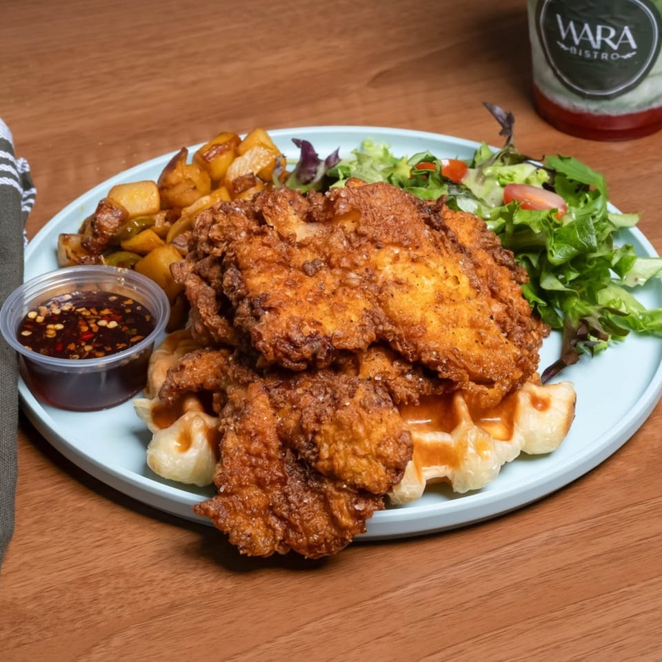 Crispy fried chicken and waffles with a side of roasted potatoes, salad, and dipping sauce.