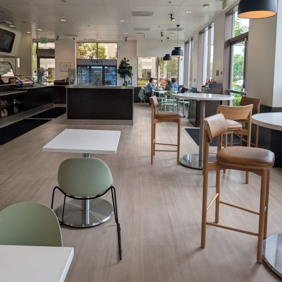 Modern cafe interior with light wood floors, various seating, and a counter with drinks.