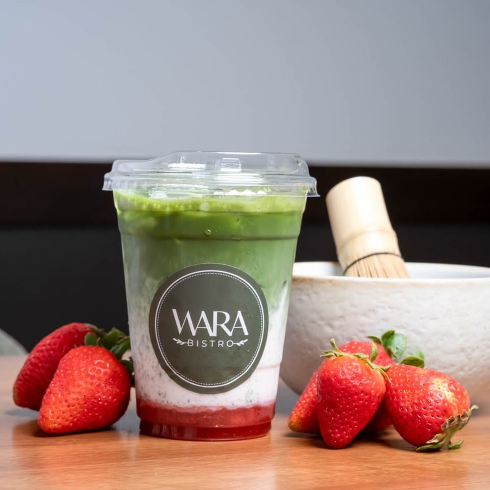 Wara Bistro's layered matcha drink with strawberries and a matcha whisk on a wooden surface.