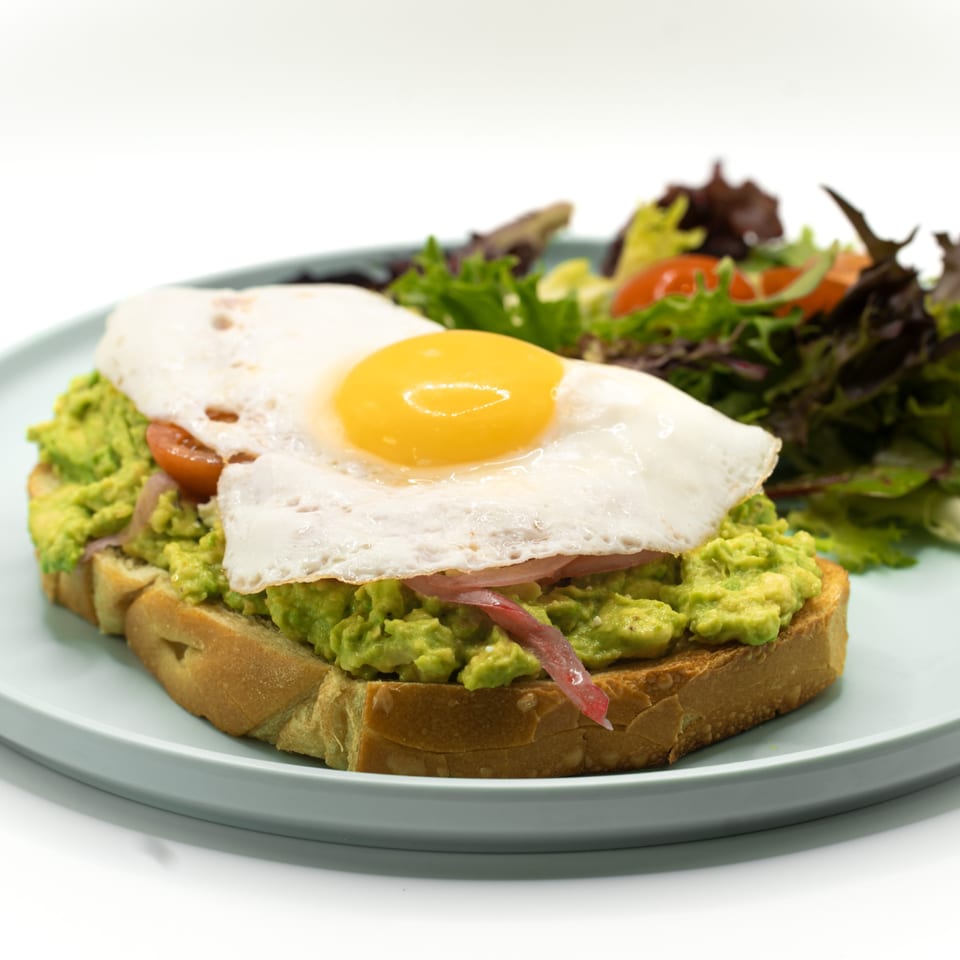 Avocado toast with a fried egg, pickled onions, and cherry tomatoes, served with a side salad.