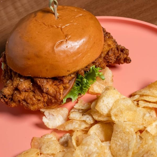 Crispy fried chicken sandwich with lettuce and tomato on a bun, served with potato chips.