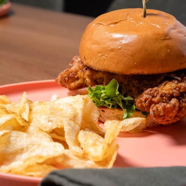 Crispy fried chicken sandwich with lettuce on a pink plate, served with potato chips.