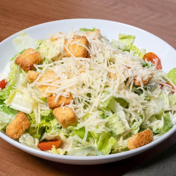 A white bowl filled with Caesar salad, topped with shredded Parmesan, croutons, and cherry tomatoes.